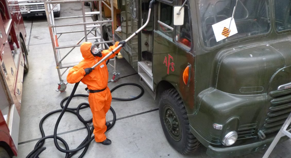 Man in orange suite removing asbestos from a vehicle