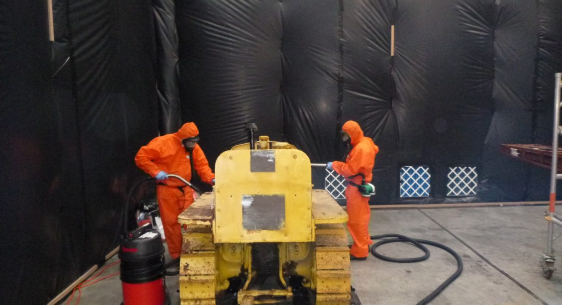 Two men in orange suites using a Vehicle Asbes Decontamination