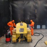 Two men in orange suites using a Vehicle Asbes Decontamination
